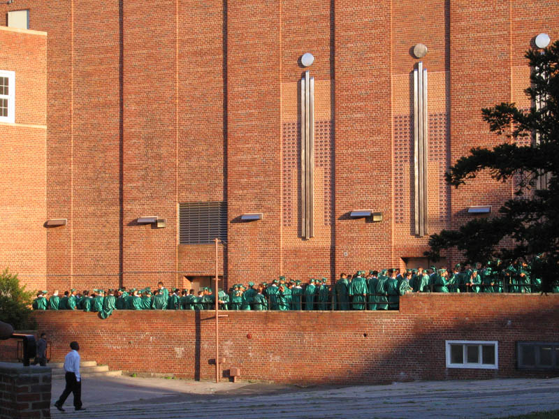 Waiting boys in green caps and gowns - girls are waiting on the other side of the building wearing golden-yellow