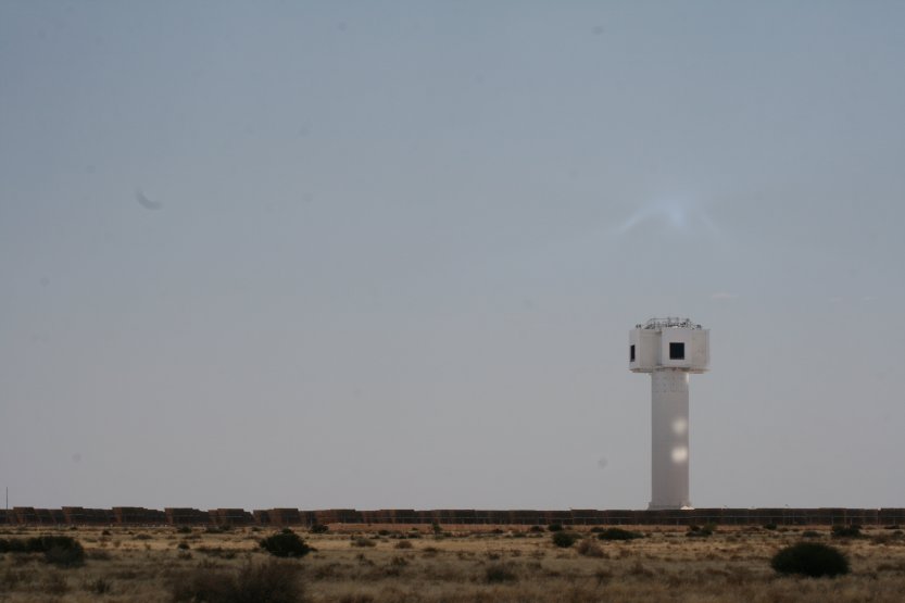 The power plant is not in operation. The sun rays are reflected either under or above. They create a light patch on a clear sky above the tower.