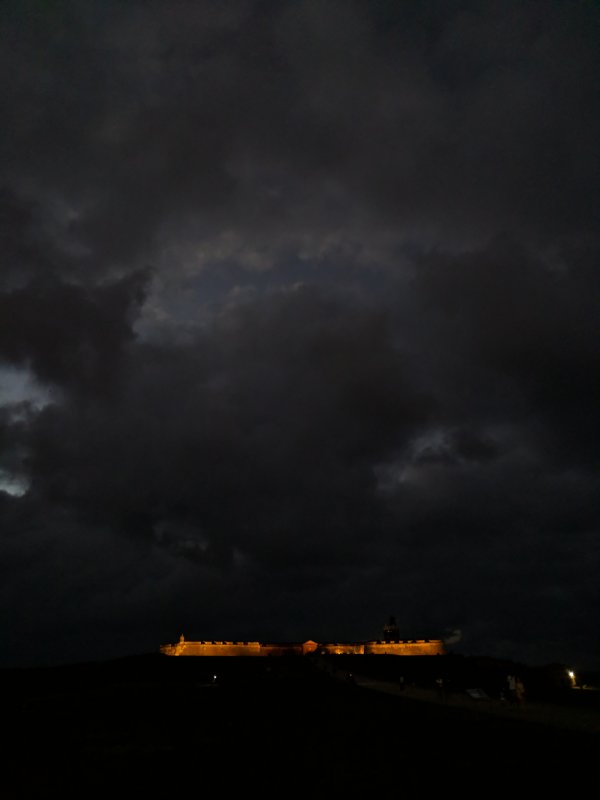 Illuminated walls of El Morro at a far distance, under the upcoming storm clouds.